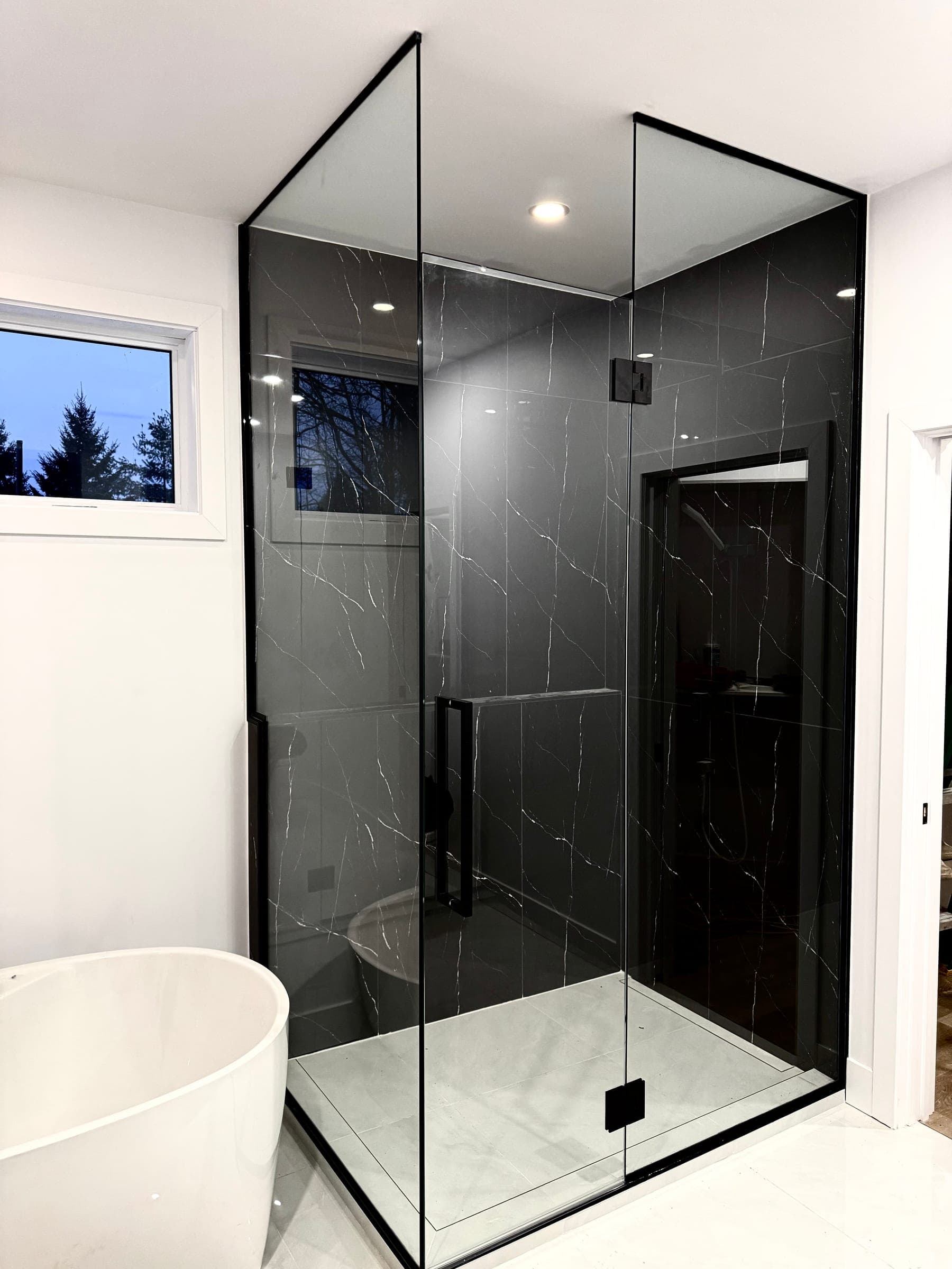 Douche d'angle à cadre noir fin sur marbre noir veiné, avec baignoire autoportante blanche
