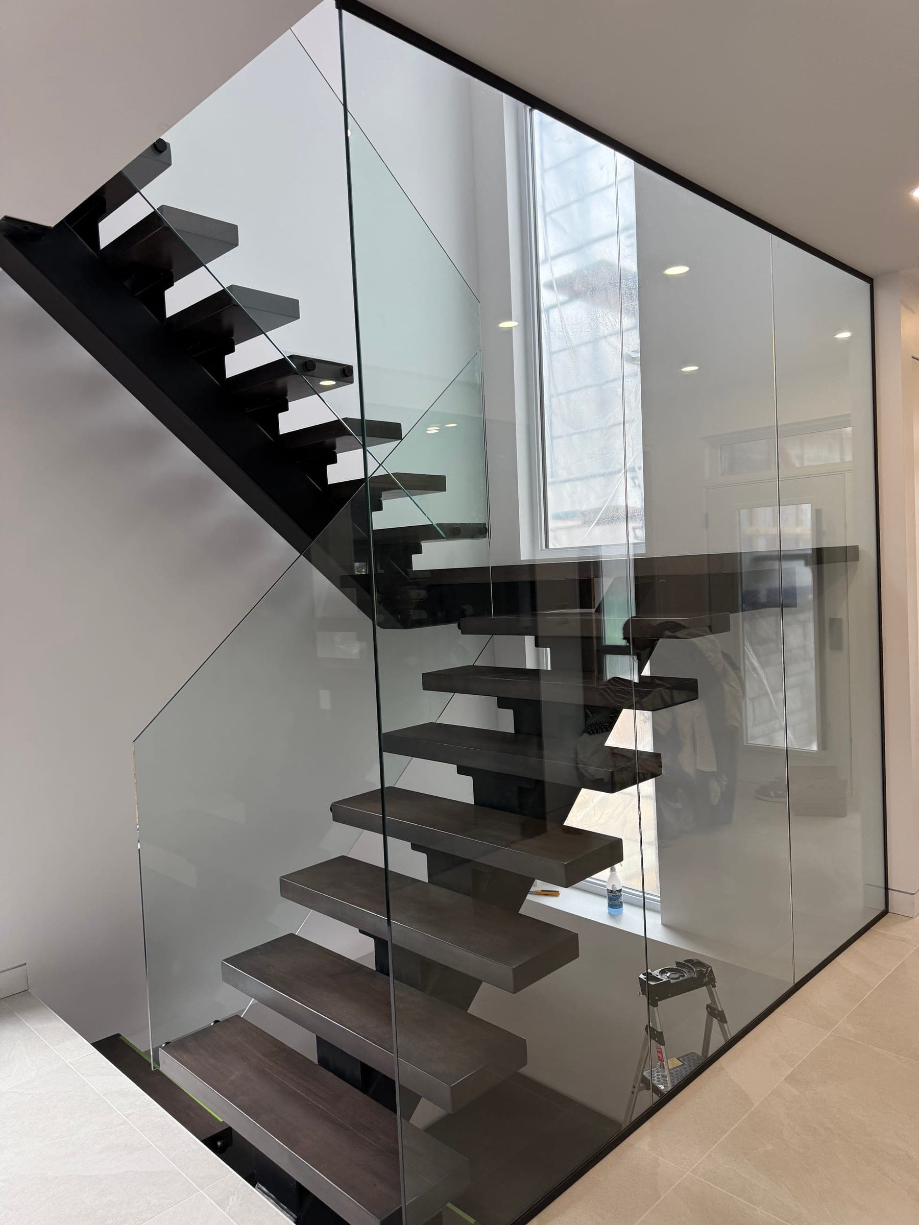 Escalier suspendu en bois foncé entièrement enfermé dans une cage de verre sans cadre, sur deux étages